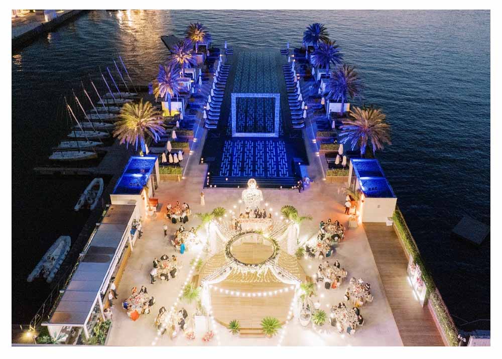 Luxury waterfront destination celebration at night with elegant lighting, curated seating, and private guest tables by the water.