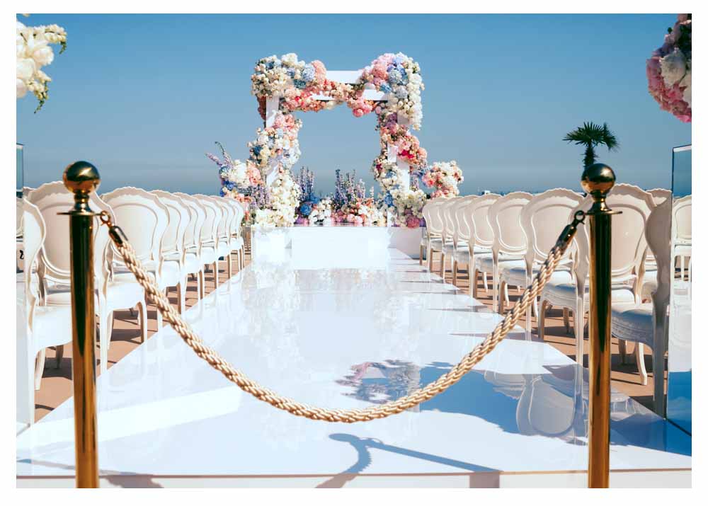 Elegant private destination ceremony setup with white chairs and floral arch overlooking the sea.